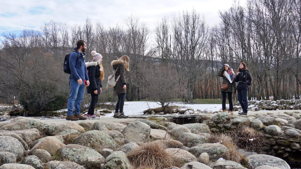Grupo de personas caminando en la naturaleza invernal, sobre un puente de piedras rodeado de nieve, en una ruta guiada por Tembo Tour.