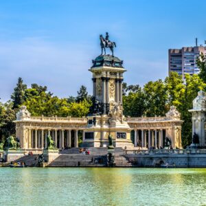 Monumento a Alfonso XII reflejado en el estanque del Parque del Retiro de Madrid, con visitantes y barcas navegando