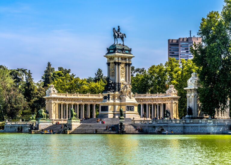 Monumento a Alfonso XII reflejado en el estanque del Parque del Retiro de Madrid, con visitantes y barcas navegando