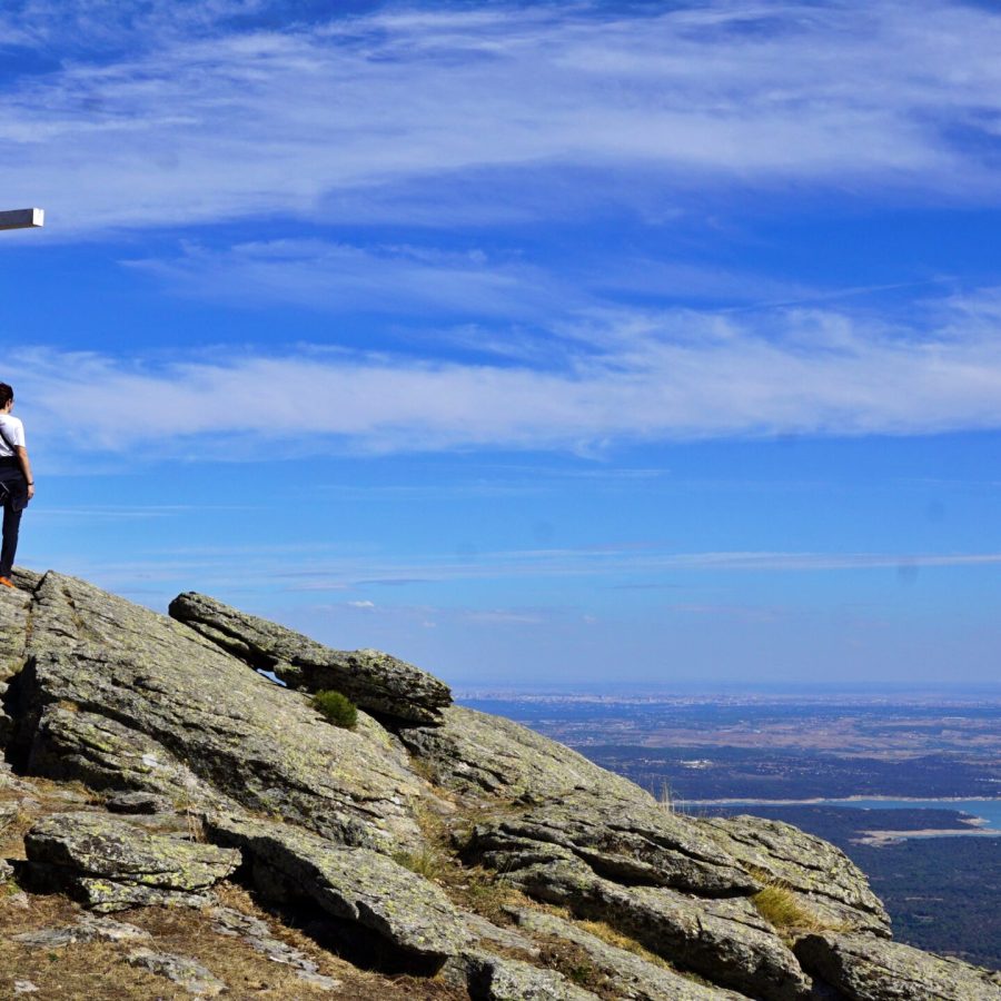 Excursionista junto a la cruz del Mirador de los Poetas en la cima de la sierra, con el embalse al fondo.