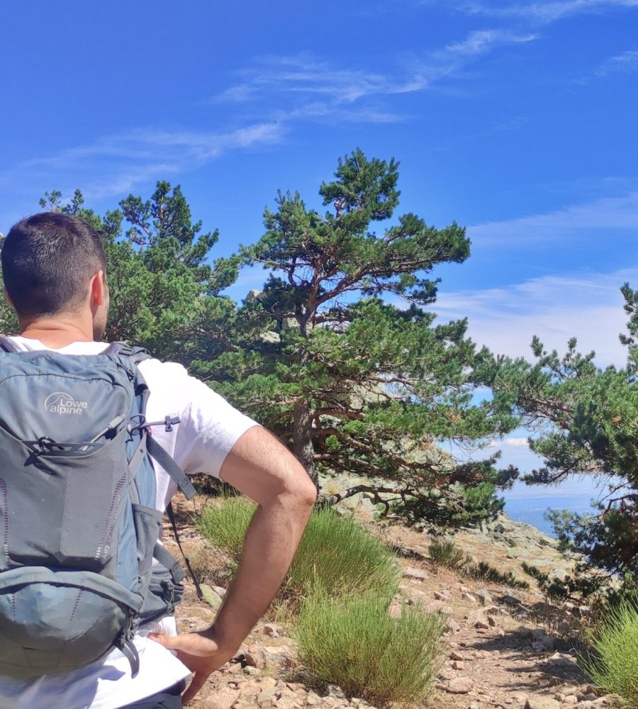 Senderista con mochila observando un vértice geodésico en la montaña.