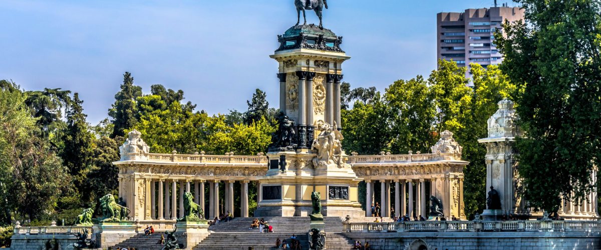 Monumento a Alfonso XII reflejado en el estanque del Parque del Retiro de Madrid, con visitantes y barcas navegando